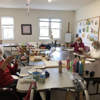 A group of people engaging in an art class, painting and crafting together around a table.