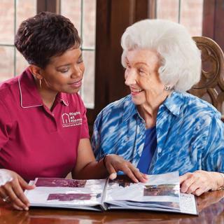 A caregiver and an elderly woman looking at a photo album together.