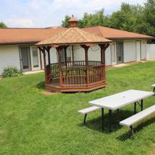A charming gazebo situated in a grassy yard next to a picnic table with a building in the background.