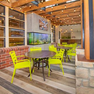A cozy outdoor cafe area with bright yellow chairs and a wooden ceiling adorned with string lights.
