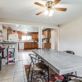 Open layout dining area with a view of the kitchen, featuring a long table and ceiling fan.