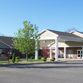 A building with an entrance and parking lot surrounded by trees and landscaping on a clear day.