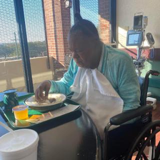 An elderly man in a wheelchair enjoys his meal in a care facility.