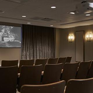 An empty theater room with rows of chairs facing a projection screen.