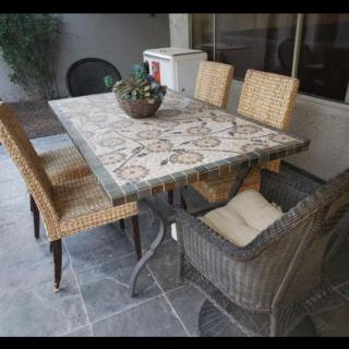 An outdoor patio setting with a mosaic dining table surrounded by wicker chairs and adorned with a potted plant centerpiece.