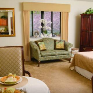 A cozy bedroom with a comfortable sofa and armchair, featuring elegant furniture and a large window with curtains.