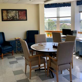 A cozy room with a round table surrounded by chairs, bathed in sunlight from large windows.