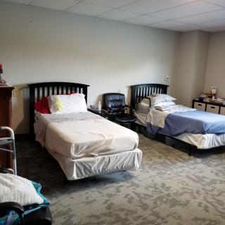 A shared bedroom with two single beds, chairs, and a nightstand in a simple setting.