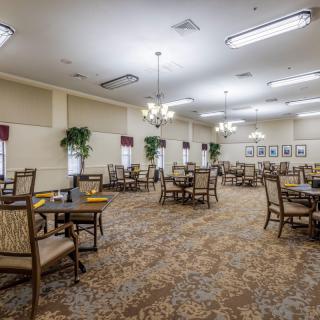 An empty dining room with tables and chairs, decorated with chandeliers and plants.