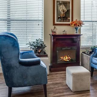 A cozy living room with blue chairs, a fireplace, and large windows.