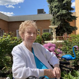 An elderly woman enjoying a peaceful moment in a beautiful garden filled with vibrant flowers.