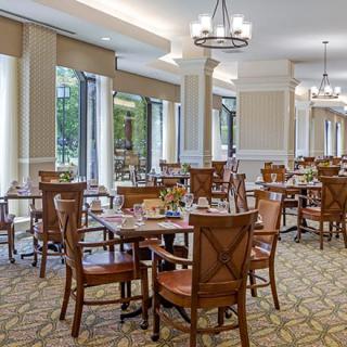 An elegant dining room with wooden tables and chairs, filled with natural light.