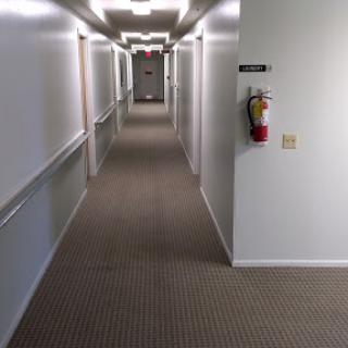 A well-lit hallway with a carpeted floor and a visible fire extinguisher.