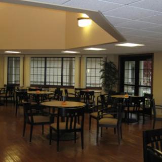 An empty cafe with wooden tables and chairs, featuring large windows and indoor lighting.