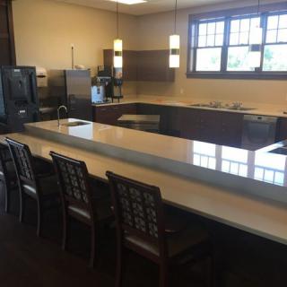 A modern kitchen with a long countertop, several chairs, and appliances.