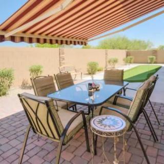 A well-furnished patio with a table and chairs, shaded by an awning in a sunny backyard.