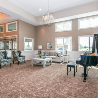 A spacious living room with elegant furnishings, featuring a grand piano, chandelier, and large windows.