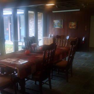 A cozy dining room with a long wooden table and chairs, illuminated by natural light through large windows.
