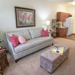 A cozy living room with a patterned sofa, colorful cushions, and an adjacent kitchenette.