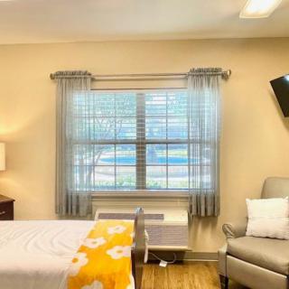 A cozy bedroom with a large window, bed, armchair, and wall-mounted TV.