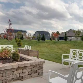 A serene patio area with white chairs and a landscaped garden, set against the backdrop of houses and a cloudy sky.