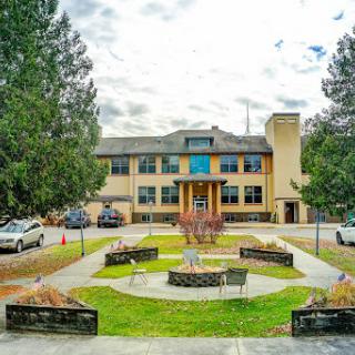 A spacious building surrounded by a well-maintained courtyard and trees, under a cloudy sky.