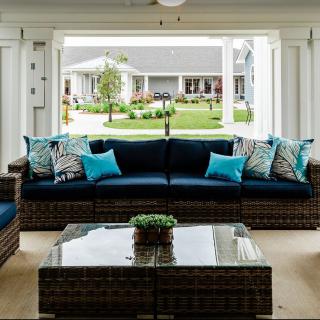A cozy outdoor seating area with wicker sofas and colorful cushions, offering a view of a lush garden through open doors.