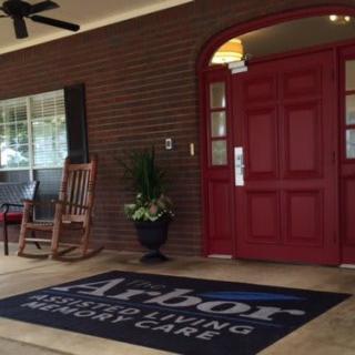 Front entrance of an assisted living facility with rocking chairs and a welcome mat.