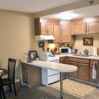 A cozy apartment kitchen with wooden cabinets, a stove, and a small dining area.