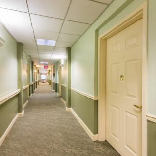 A long, carpeted hallway with doors on either side and overhead ceiling tiles.