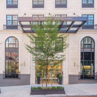 Elegant building entrance with large glass windows and a central tree.