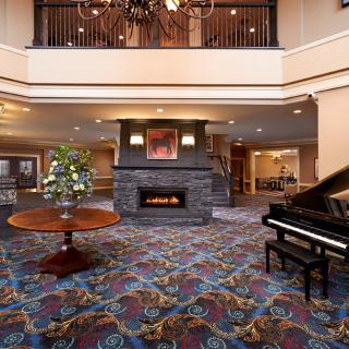 A spacious hotel lobby featuring a grand piano, a stone fireplace, and elegant decor.