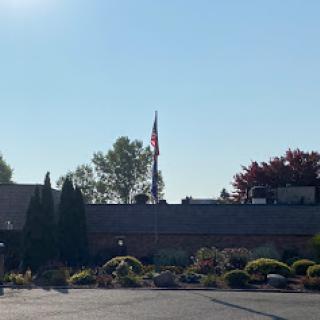 A clear day featuring a flag atop a building, surrounded by manicured landscaping.