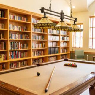 A cozy library room with a pool table and bookshelves lining the walls.