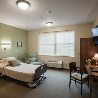 A well-lit hospital patient room featuring a bed, seating area, and a desk.