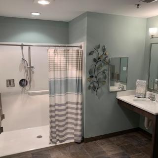 A modern and accessible bathroom featuring a walk-in shower with a striped curtain, a mirror above the sink, and neatly arranged towels.