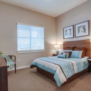 A cozy bedroom with a neatly made bed, nightstand with a lamp, and art pieces on the wall.