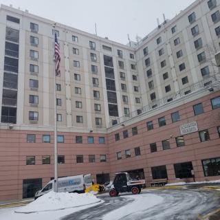 A view of a multi-story hospital building with an American flag, surrounded by snow.