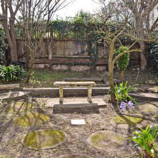 A serene garden featuring a stone bench, surrounded by trees and blooming flowers.