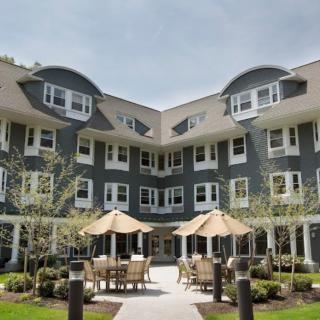 A modern residential building with outdoor seating and umbrellas in the courtyard.