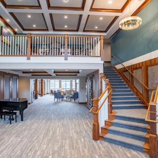 A spacious and elegant lobby featuring a grand staircase and a piano, designed with modern aesthetics and warm wood accents.