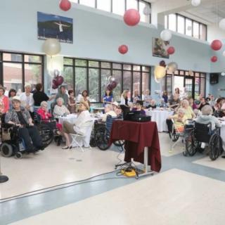 A group of people gathered indoors at an event, with many attendees in wheelchairs and festive decorations adorning the space.