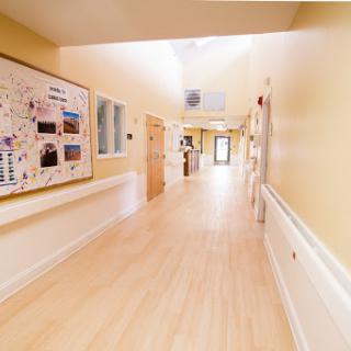 A bright and clean hallway in a healthcare facility, featuring light-colored walls and wood flooring.