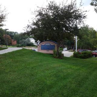 A grassy area with a signboard and trees in a suburban setting.