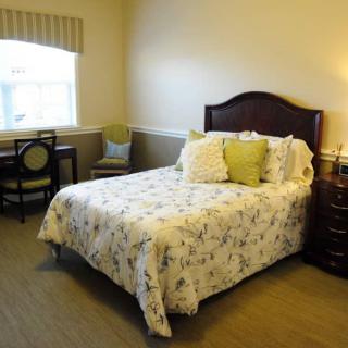 A cozy bedroom with a neatly made bed, adorned with decorative pillows, a bedside lamp, and a window letting in natural light.