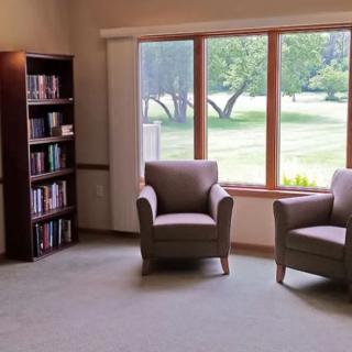 A cozy reading area with two chairs by a window, alongside a bookshelf filled with books.