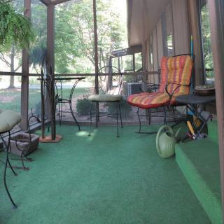 A cozy screened porch with colorful chairs, a green carpet, and plants, perfect for relaxing.