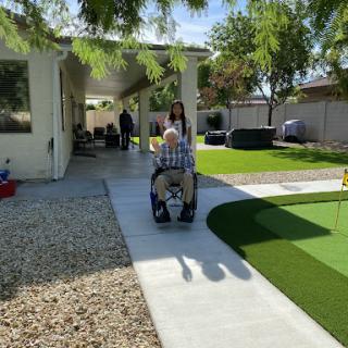 A senior individual using a wheelchair on a sunny day in a well-maintained garden.