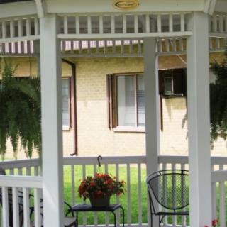A cozy gazebo with a chair and potted plants, surrounded by greenery.