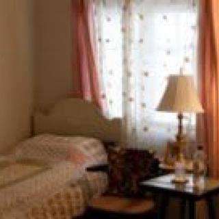 A cozy bedroom with a single bed, bedside table, and lamp by the window.